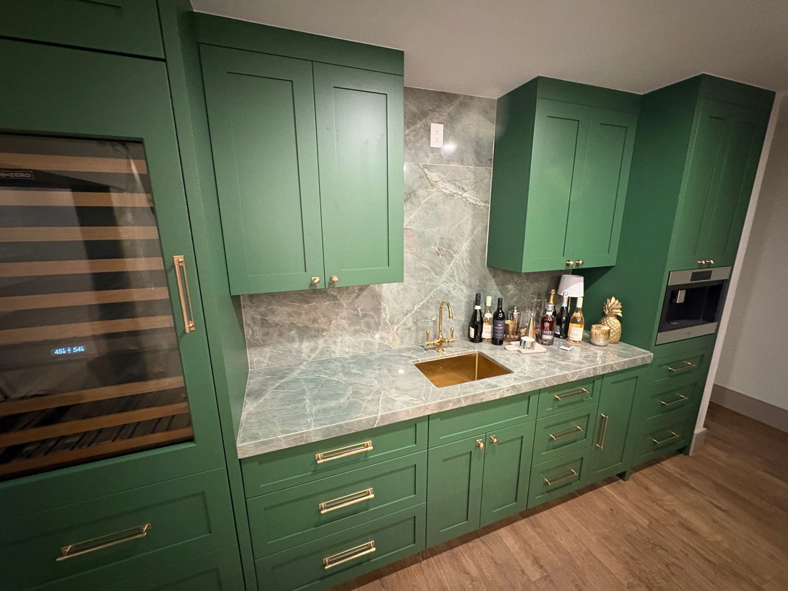 Custom home bar with brass sink, quartzite backsplash and green shaker cabinets