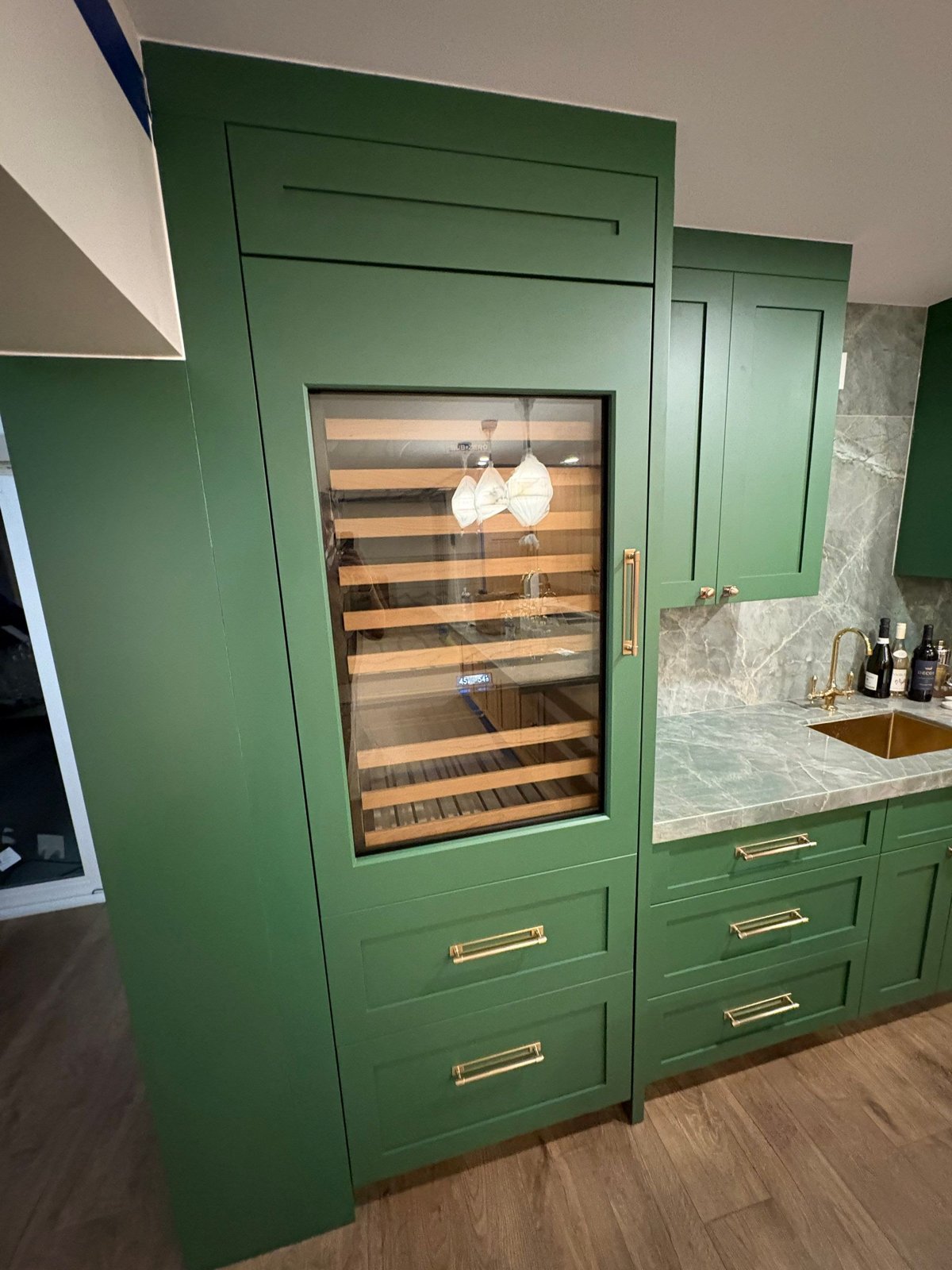 Glass-front wine column with oak racking built into green custom cabinetry