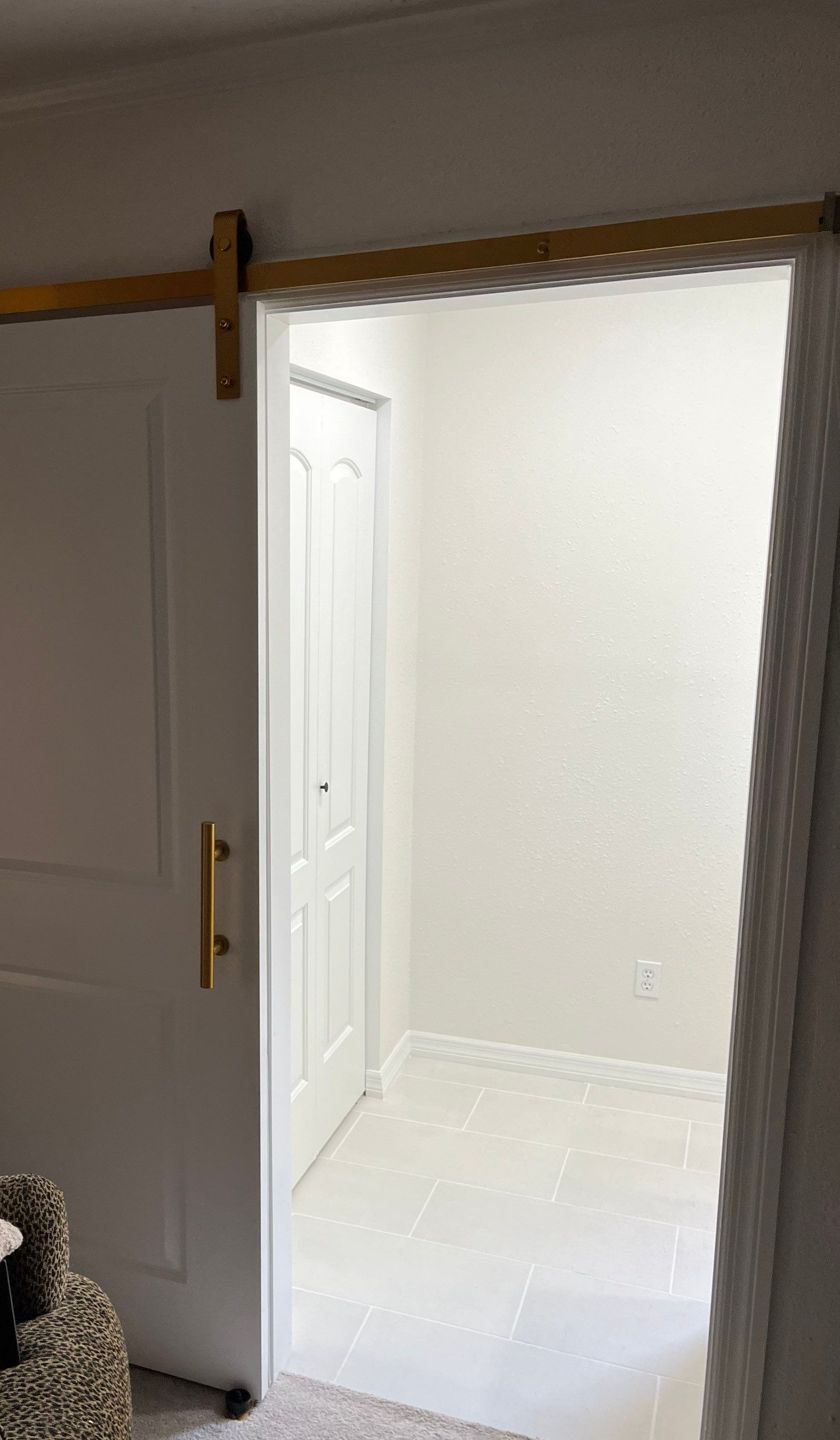 Sliding barn door with brass track at the entry to a remodeled master bathroom