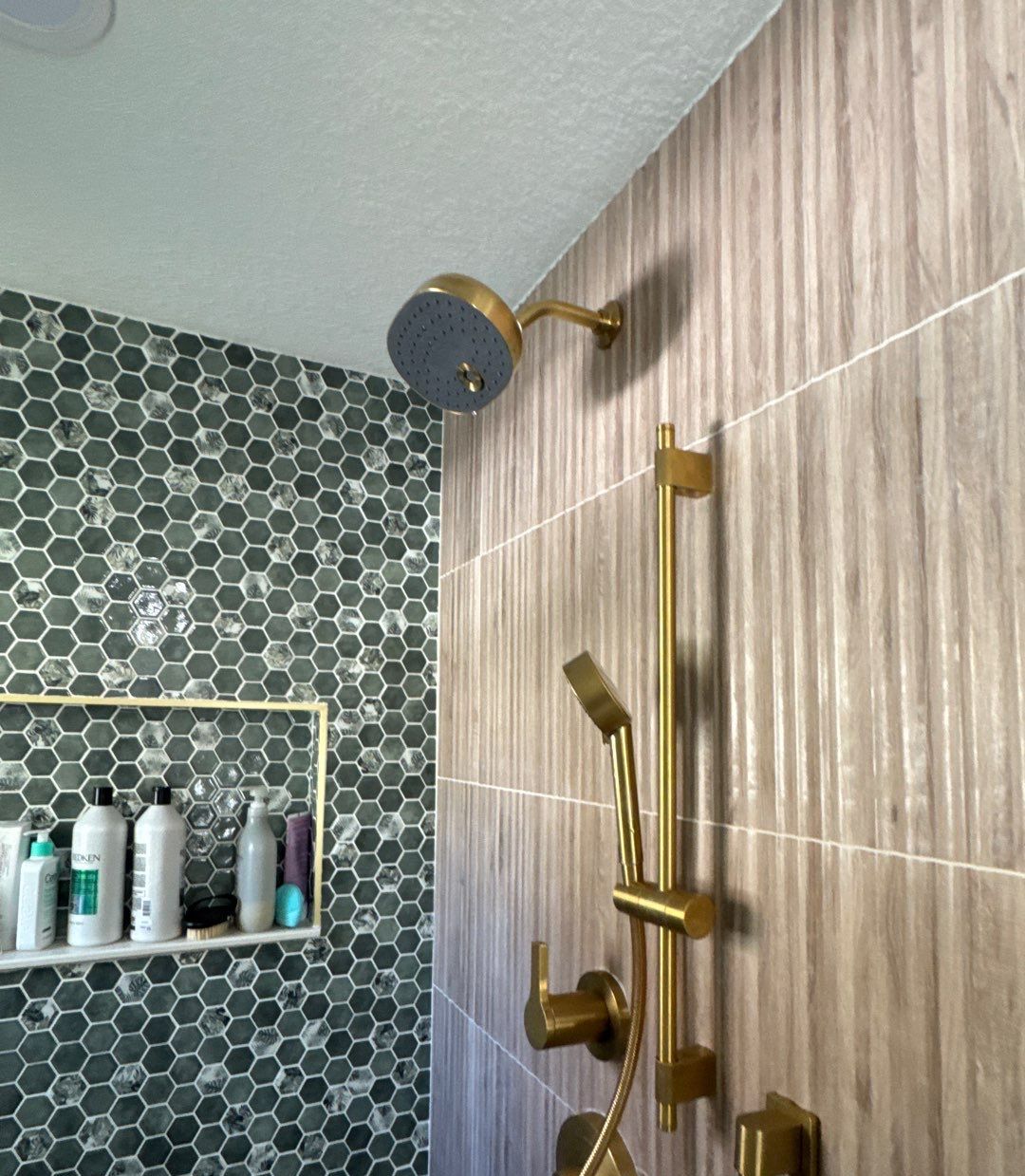 Brass rain shower head, slide bar and hand shower on wood-look tile