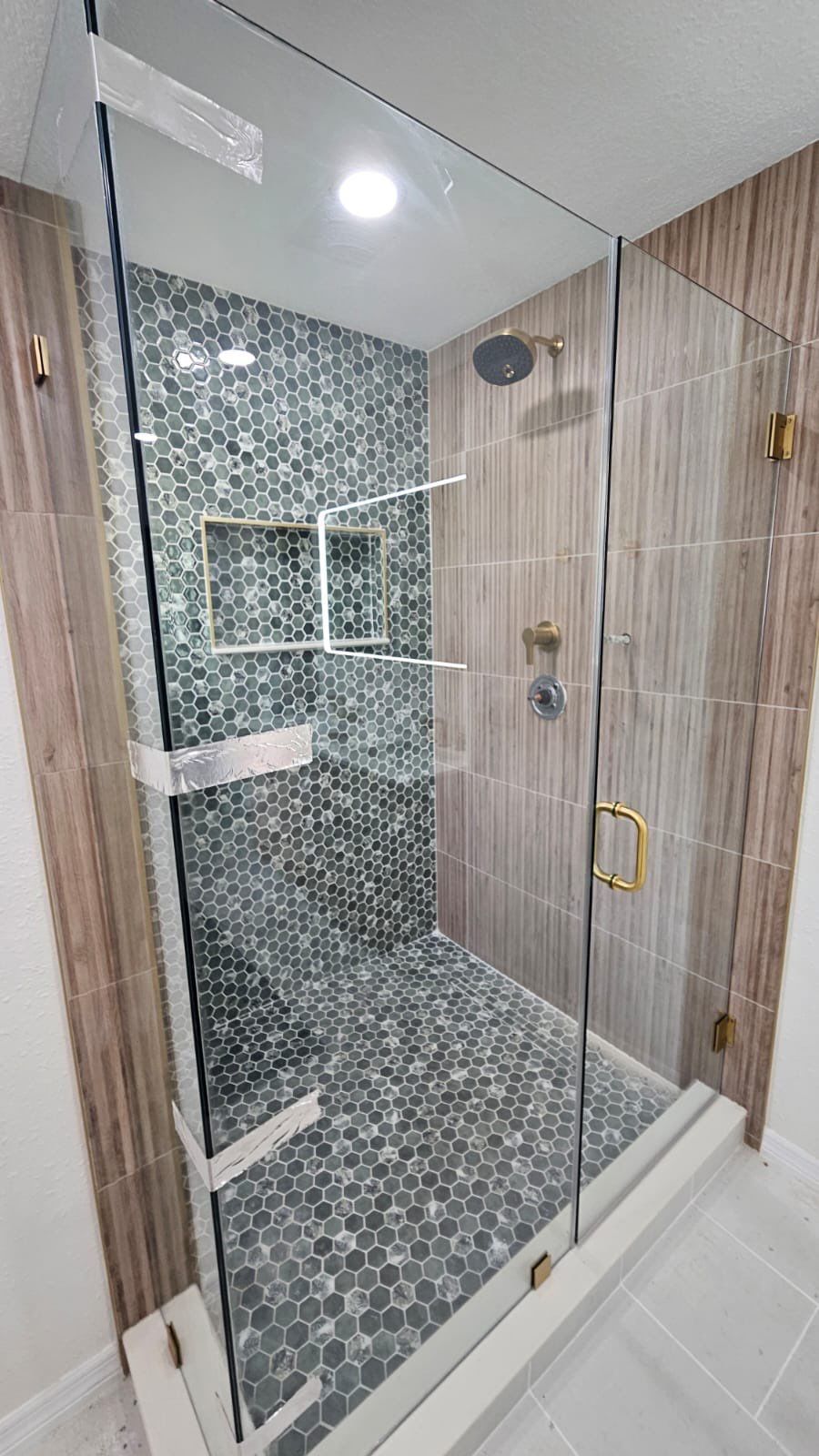 Frameless glass shower enclosure with green hexagon tile and wood-look wall tile